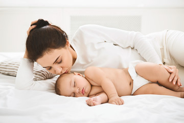 Obraz na płótnie Canvas Mother kissing her sleeping newborn baby in bed