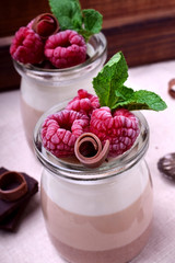 Three chocolate mousse dessert in a glass jar garnished with frozen raspberries and mint