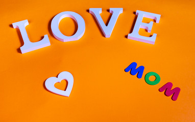 Word love in white and also white heart and colored word mom over orange background