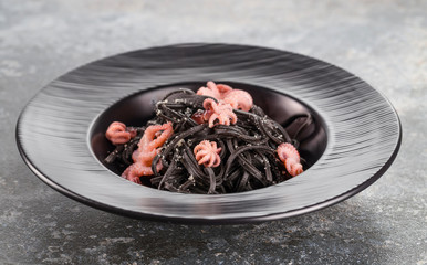 Black spaghetti with octopus and Parmesan cheese on a black plate.