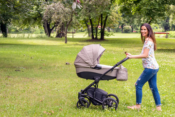 A beautiful young mother walking with her baby in a stroller in the park on a sunny day.