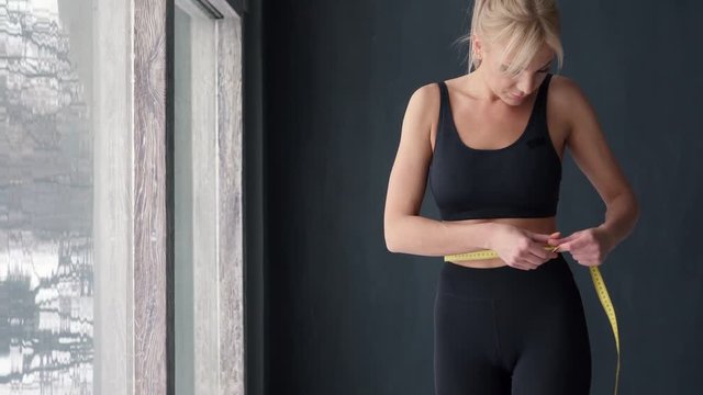 slim woman measuring waist with tape measure in centimeters