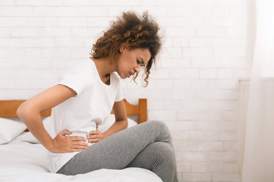 Unhappy woman suffering from stomachache, sitting on bed