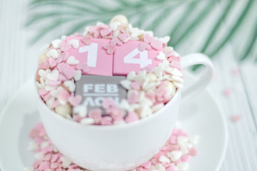 Pink square wood with white numbers 1 and 4.Gray square wood with white letters FEB.February 14 Valentine's Day.White coffee cup on wooden floor.Many small hearts, white and pink.
