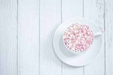 White coffee cup on wooden floor.Many small hearts, white and pink, are in a cup of coffee.Pink square wood with 1 and 4 white numbers, white glass..