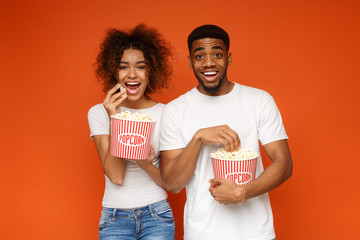 Man and woman eating popcorn on orange background