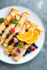 Sweet pancakes wrapped with fresh berries, crepes with blueberry and raspberry on breakfast, top view
