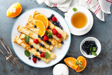 Sweet pancakes wrapped with fresh berries, crepes with blueberry and raspberry on breakfast, top view