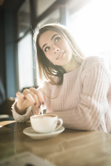 Young pretty woman holding coffee spoon and stirring hot coffee on wooden table.