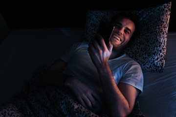 Young man using smartphone in bed at night