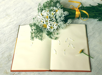 greeting card / A bouquet of chamomiles  and an open  notebook    on a white wooden background.
