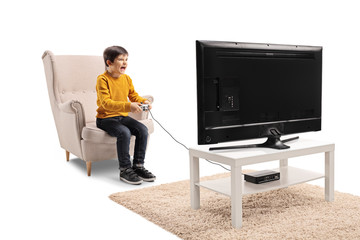 Young boy sitting in an armchair in front of a TV and playing video games