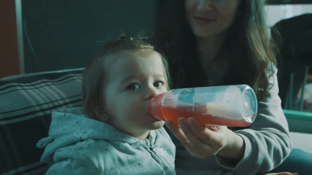 Smiling baby gerl lying down while drinking tea from a bottle