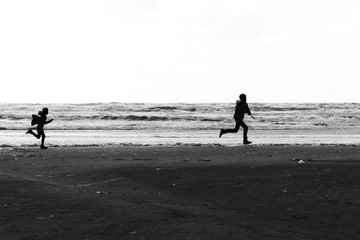 Fototapeta na wymiar Silhouettes of a brother and a sister running wild and free at the beach