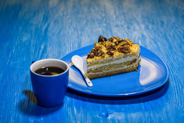 Sponge cake with walnuts, near a cup of coffee on wooden background.
