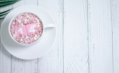 Fototapeta na wymiar Pink square wood with white numbers 1 and 4.Gray square wood with white letters FEB.February 14 Valentine's Day.White coffee cup on wooden floor.Many small hearts, white and pink.