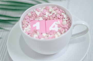 Pink square wood with white numbers 1 and 4.Gray square wood with white letters FEB.February 14 Valentine's Day.White coffee cup on wooden floor.Many small hearts, white and pink.