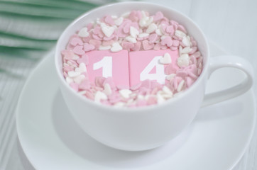 Pink square wood with white numbers 1 and 4.Gray square wood with white letters FEB.February 14 Valentine's Day.White coffee cup on wooden floor.Many small hearts, white and pink.