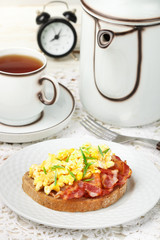 Bread toast with scrambled eggs, fried bacon and green onions.  Delicious breakfast. Brunch. Selective focus