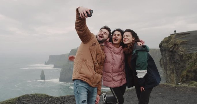 Closeup happy friends taking pictures in amazing place with beautiful landscape with a big Cliffs , they smiling large , they using a smartphone to take pictures. 4k