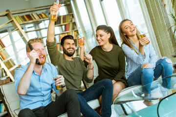 Group of young friends looking at the TV, drinking cider and having fun  in the room