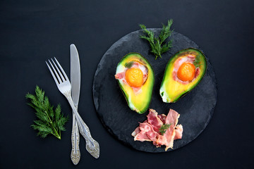 tasty baked avocado with an egg on a black background