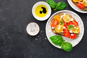 Healthy food. Cherry tomatoes, cottage cheese, young cheese, basil sandwiches, wholegrain bread with olive oil, balsamic sauce. Top view, space. On a gray dark background..