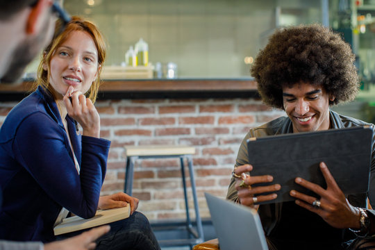 Afro american man talking smiling with colleagues or clients using tablet.Group of multiethnic people having business team meeting in restaurant lounge.Teamwork,corporate,diversity and social concepts