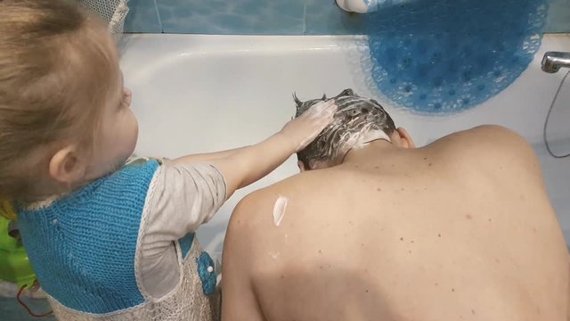 little girl shampoos her father's head in the bathroom