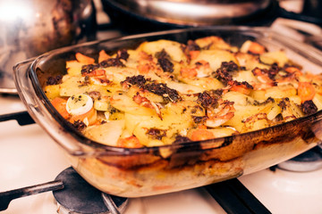 Potato baked with carrots, onions, eggs, chicken meat and sprinkled with cheese on top in a glass vessel at home