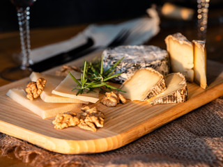 Some kinds of the blue cheeses with halves of the walnuts and rosemary, two glasses with red wines, knife and fork on the wooden desk