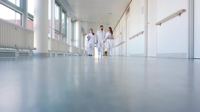 Doctors, two women and a man, in hospital walking down the corridor
