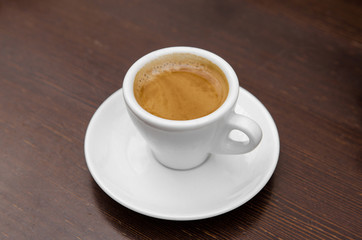 White cup with coffee on a white saucer on a wooden table