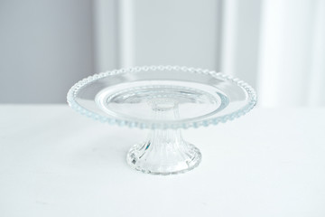 The glass round stand is decorated with glass balls for cake and desserts on a white table on a...