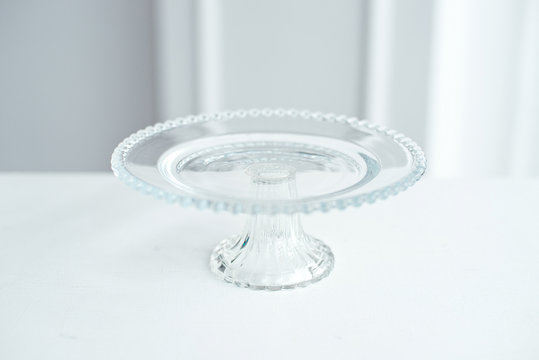 The glass round stand is decorated with glass balls for cake and desserts on a white table on a white background.