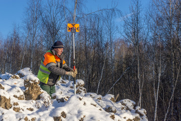 A surveyor's assistant with a measuring instrument conducts a topographical survey for cadastre