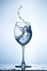 Splashing water on blue background. Wine glass with water.