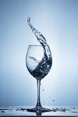 Splashing water on blue background. Wine glass with water.