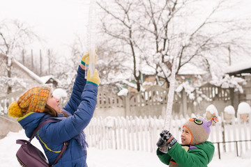 Children play with icicle in snow. Outdoor fun in snowy park by cold weather.