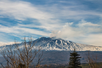 A beautiful view of the eruption of volcano Etna with smoke and snow is in the photo in winter in Sicily