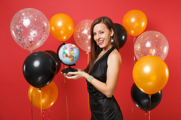 Beautiful smiling young woman in little black dress celebrating, holding world globe on bright red background air balloons. St. Valentine's Day, Happy New Year, birthday mockup holiday party concept.