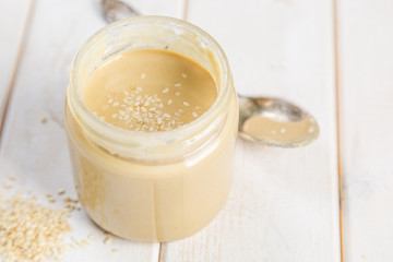 Obraz na płótnie Canvas Sesame seeds butter in glass jar, white wood background