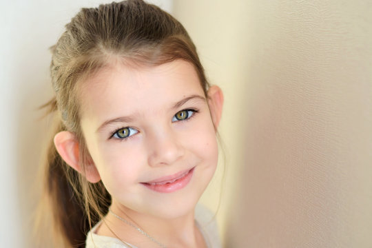 portrait of a little caucasian white beautiful brunette girl with pony tail on neutral background. smiling toothless green eyed happy girl with cute protruding ears. Kid expression portrait with fun h