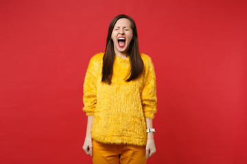 Portrait of weird crazy young woman in yellow fur sweater keeping eyes closed screaming isolated on bright red wall background in studio. People sincere emotions lifestyle concept. Mock up copy space.