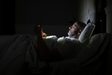 Fototapeta na wymiar Man using his phone in his bed instead of sleeping, technology addiction concept