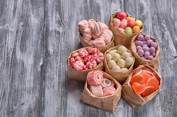 Colored candy in paper bags on wooden background