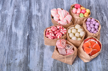 Colored candy in paper bags on wooden background
