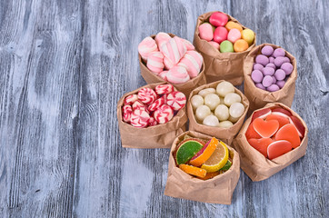 Colored candy in paper bags on wooden background