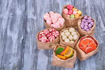 Colored candy in paper bags on wooden background