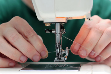 Close-up seamstress hands working on sewing machine at home. Sewing process. woman hands behind sewing close-up. The process of threading into the needle.